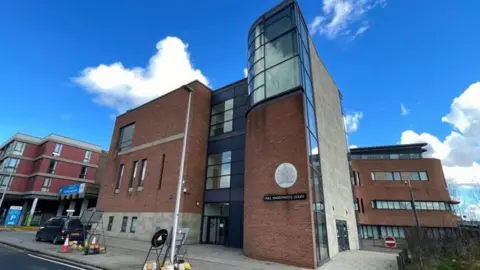 Hull Magistrates' Court is a large red-brick and glass building under a cloudy blue sky.