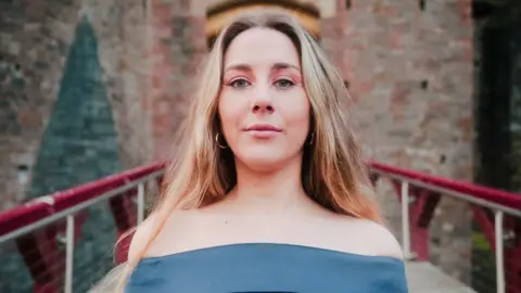 A woman with long blonde hair in a dress standing in front of a castle