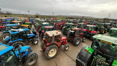 Somerset Tractor Runners Rows and rows of blue, green, red and yellow tractors parked in a large concrete yard. 