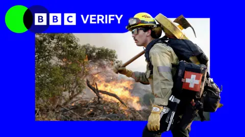 A firefighter with an axe stands in front of burning scrub in southern California