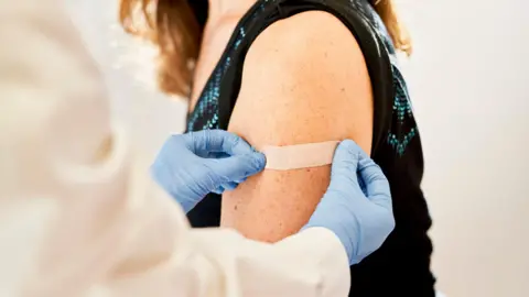 Getty Images Doctor applying band-aid to a patient, whose look   cannot beryllium  seen, aft  receiving the 3rd  dose of vaccine for immunization - banal  photo