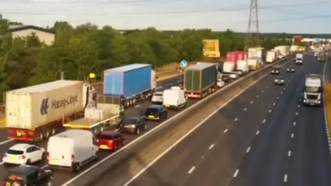 Highways England A blurry traffic camera picture of queuing traffic on the M25 near junction 25. The traffic is queuing on the left side heading to the right . The lanes on the right side are free-flowing. 
