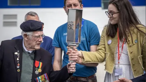 CHRISTOPHE PETIT TESSON/EPA-EFE/REX/Shutterstock British WWII veteran Jim Grant (L) holds the 'Torch of Commemoration' with a French member of the Commonwealth War Graves Commission at their arrival at Caen-Ouistreham ferry terminal