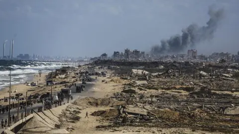 Anadolu via Getty Images Smoke rises from ongoing strikes as Palestinians, carrying their belongings by vehicle or on their backs, continue to flee toward southern Gaza via al-Rashid Street after intensified Israeli attacks and ground operation amid forced evacuation orders in Gaza City, Gaza on September 26, 2025
