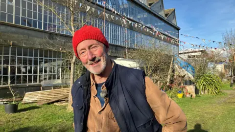 Chris Black standing in front of the Zig zag building wearing a red woollen hat