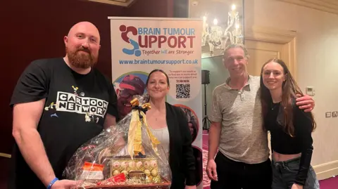 BHA A group of four men and two women from the Bristol Hoteliers Association stand smiling at the camera with their prize - a plastic wrapped bag full of chocolates and other items - for winning a charity quiz