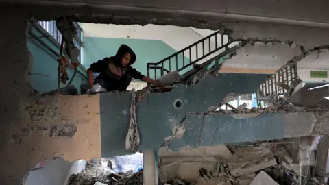 Reuters The interior of a building, damaged walls and rubble. A teenage boy looks down at the damage. 