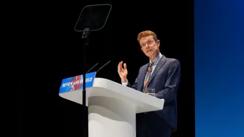 Andy Street behind a white lectern with the words "Review and Rebuild" written on it