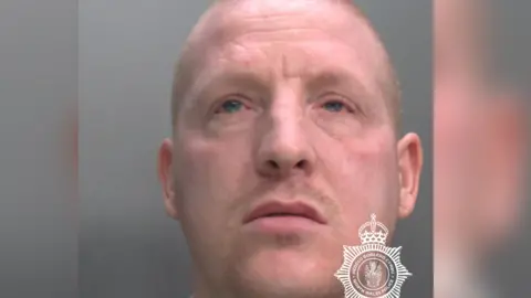 A mugshot of Lee Mullen who has a shaven head and is looking upwards while facing the camera