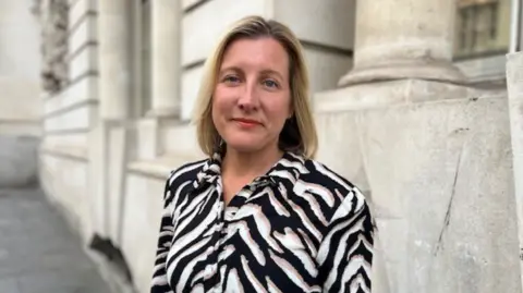 A woman in a zebra-stripped shirt stands outside of a white stone building.