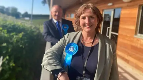 BBC Janet Finch-Saunders smiling with a blue rosette attached to her lapel. 