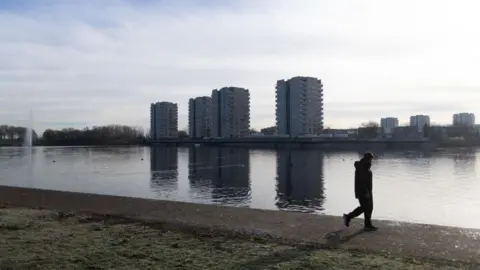 Getty Images A group of residential tower blocks overlook and artificial lake. A man is walking along the lake in the foreground. 