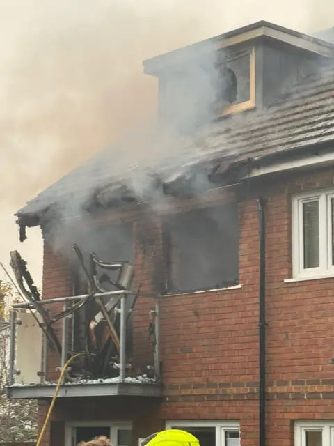 London Fire Brigade Handout from the LFB showing the house's burnt roof and smoke coming out of broken windows and debris falling off a balcony. 