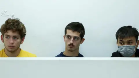 Belgium nationals David Lornoy, wearing a yellow T-shirt and Seppe Lodewijckx, wearing a black T-shirt sitting next to Vietnamese national Duh Hung Nyugen who is wearing mask 