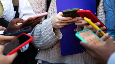 A close up of a group of people using mobile phones - their hands and the phones are visible. 