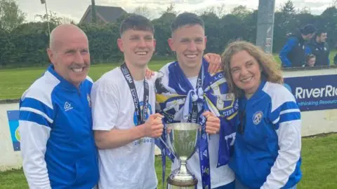 Sharon Boorman Left to right Mark, Tiarnán, Ruairi and Sharon Boorman. 
Mark is wearing a blue and white Limavady United tracksuit top and Sharon is wearing similar. Both Tiarnán and Ruairi are holding on to a trophy, while Ruairi is draped in a Limavady United flag