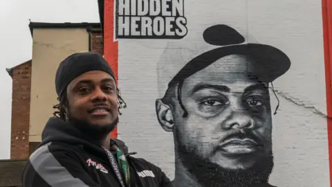 LoveBrum Malachi Nunes posing next to a street art mural celebrating his charity Ambitious Lives