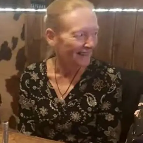 Merseyside Police Rose Johnston, who is sitting at a restaurant table in front of a small birthday cake and candle, with her hair tied back and wearing a black patterned blouse. 