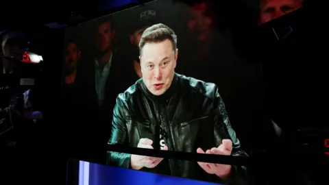 Elon Musk addresses supporters wearing a leather jacket speaking into a microphone ahead of SpaceX's launch on the Nasdaq stock exchange. 