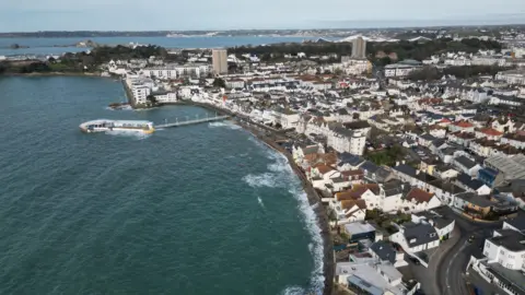 An aerial view of Harve des Pas. it shows the coastline at hightide and the surrounding area of housing. 