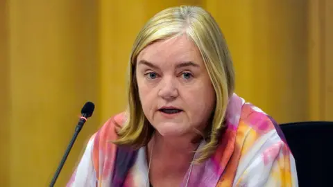 Casey in a multicoloured top talks into a microphone