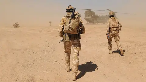 Getty Images British soldiers in uniform walk across a dusty, desert landscape towards a military helicopter near the Pimon military camp in Nad-e Ali district of Helmand province in March 2010.