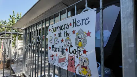 A sign outside the cafe with cartoon animals drawn on it and reading "summers here at the parklife cafe"