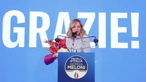 Italian Prime Minister EPA Giorgia Meloni is pictured holding a bouquet of flowers and standing in front of a sign saying Grazie (thank you in Italian) in Rome, Italy, 09 June 2024