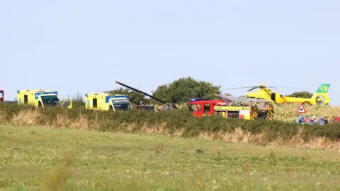 Echo/Solent Emergency service vehicles can be seen on the road near a green field