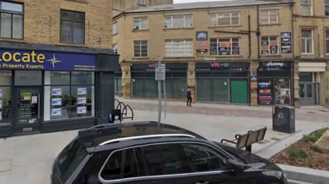 Google A black VW car parked in a parking bay on Bradford's North Parade with paving and street furniture close to it.