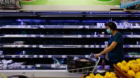 EPA A woman walks past an empty shelves after panic buyers rushed to supermarkets, after multiple local governments across the island suspended work and classes to brace for Typhoon Gaemi