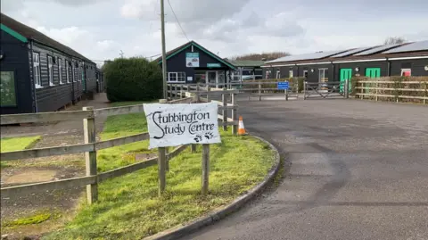 Image shows the entrance to the study centre with the sign and the reception. There are modular black cabins to the left and right. 