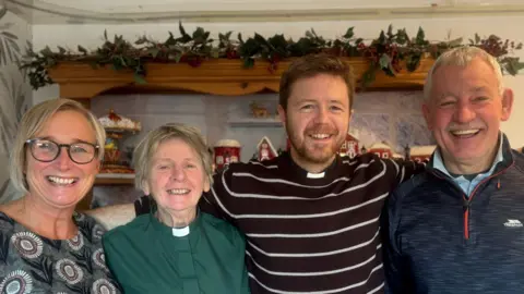 From left to right is a Lorna Brown with short blonde hair and is wearing a patterned top, Reverend Hawthorne-Steele with short hair and a green shirt with clerical collar, Reverend Chris Bennett with brown hair and beard wearing a striped shirt and clerical collar and a man with short grey hair wearing a zip-up fleece.