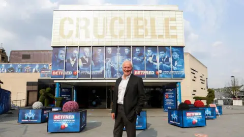 Getty Images A man wearing a black suit and white shirt with short white hair stands outside the Crucible in Sheffield