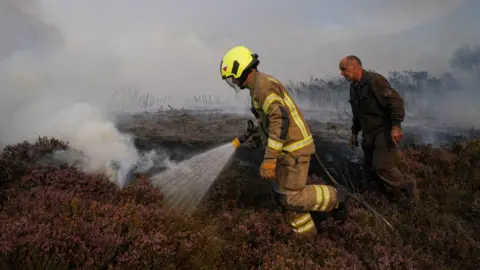 A firefighter helps combat a fire on heathland alongside the A171 road on August 14, 2025 in Fylingdales.
