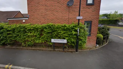 Side of brick new-build house with a street light and road sign in front. The road sign read Swinhoe Road. 
