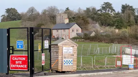 The fencing in front of the entrance to the Wolborough site with a wooden hut