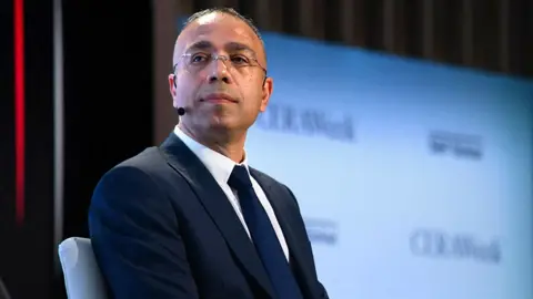 Elnur Soltanov looks to the left of camera wearing a suit and glasses with a mic attachment on his left cheek, onstage at during CERAweek oil summit in Texas in March