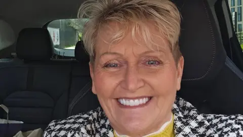 Jamiel Slaney-Summers Jamiel Slaney-Summers in a smiling selfie. She is wearing a black and white coat and a yellow and white jumper. She is sat in a car, which has black seats. She has short hair and is wearing make up. She has white, well kept teeth. 