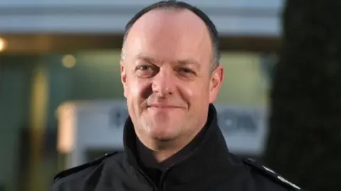 Lancashire Police Head and shoulders image of Terry Woods. He has very short dark hair, greying at the sides and is wearing a black zip up jacket