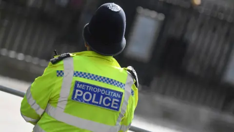 The back of a Metropolitan Police officer wearing a hi-vis jacket and hat