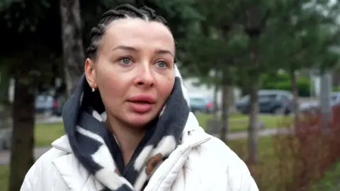 A Ukranian woman in a white coat, she has braided black hair and blue eyes