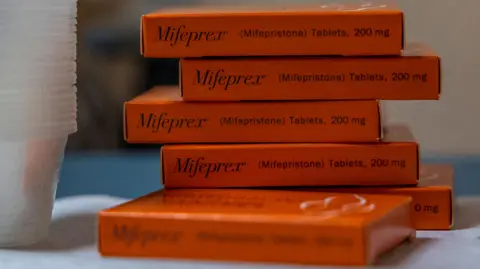 Evelyn Hockstein/Reuters A stack of orangish  tablet boxes connected  a array  with Mifepristone labelled connected  them. They are adjacent  to a stack of wide   integrative  cups. 