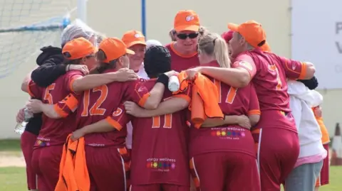 Socialball The Brighton & Hove Socialball team founded by Vanessa Hood in a huddle before a game. The team wear a maroon and orange kit.