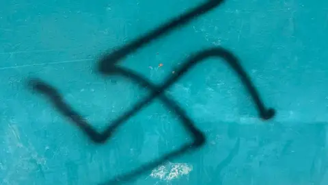 Declan Norris A swastika symbol in black spray-paint is visible on a blue background