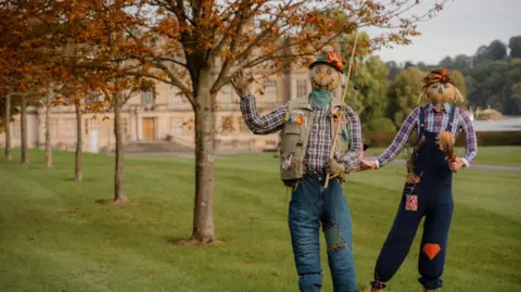 Longleat Two scarecrows in front of Longleat House in checked shirts and patched jeans with smiles and one waving to camera 