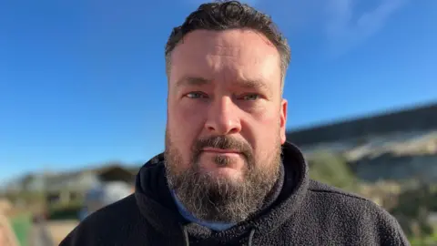 A bearded man looking at the camera with a neutral expression.