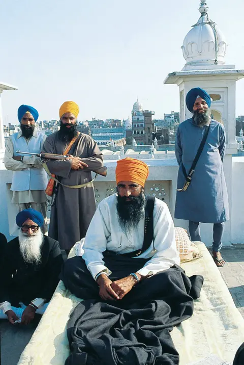 Raghu Rai / The India Today Group via Getty Images Sikh separatist leader Jarnail Singh Bhindranwale, wearing a turban ans surrounded by his armed supporters and guards, sitting on a cot.