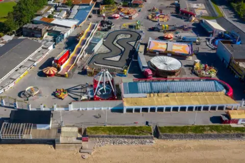An aerial view of the funfair with several rides and the beach in front.