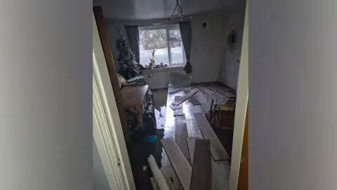 Daniel Pownall Dirty brown water and debris cover the floor of a living room.